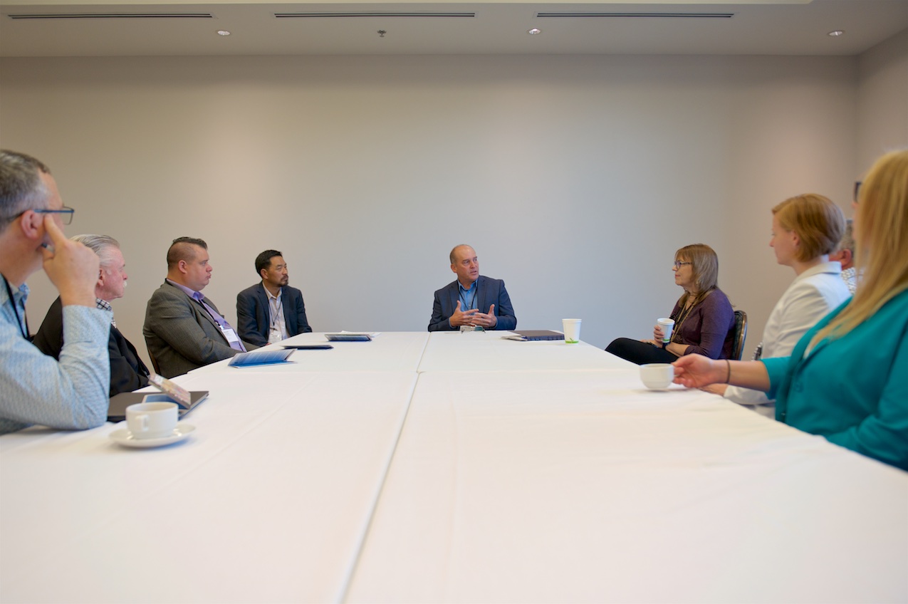Group of people in business attire sitting around a long table having a meeting.