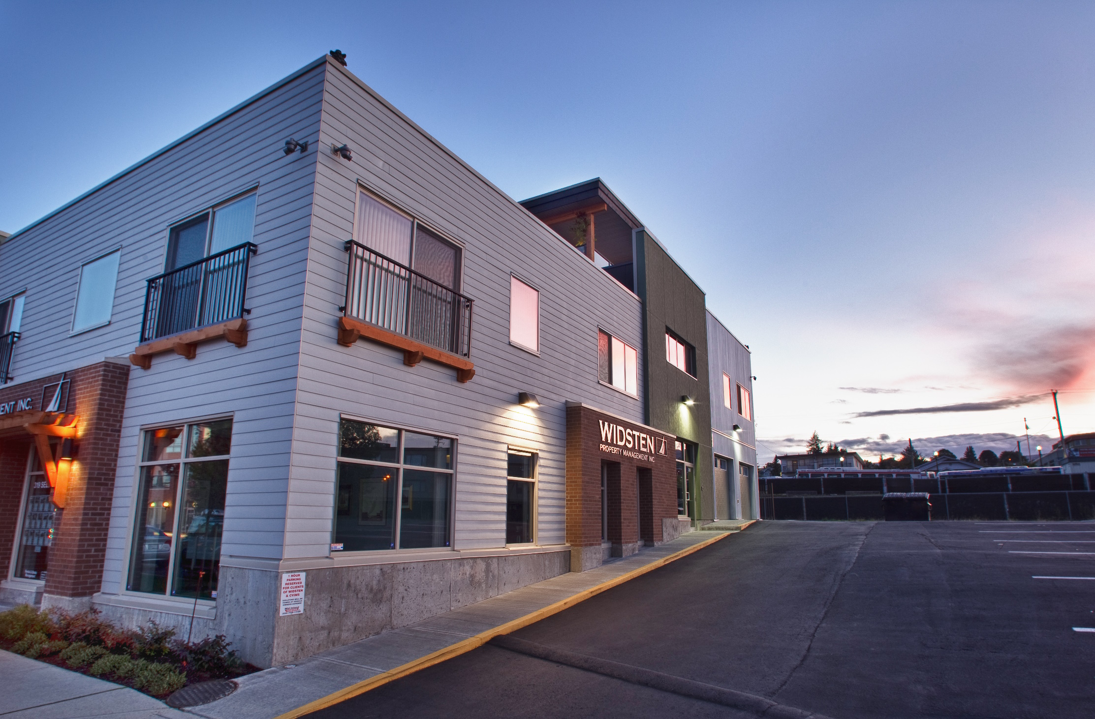 Exterior view of a modern, two-story commercial building with a mix of white and grey siding. The building features balconies with black railings and is labeled with 'WIDSTEN Property Management Inc.'