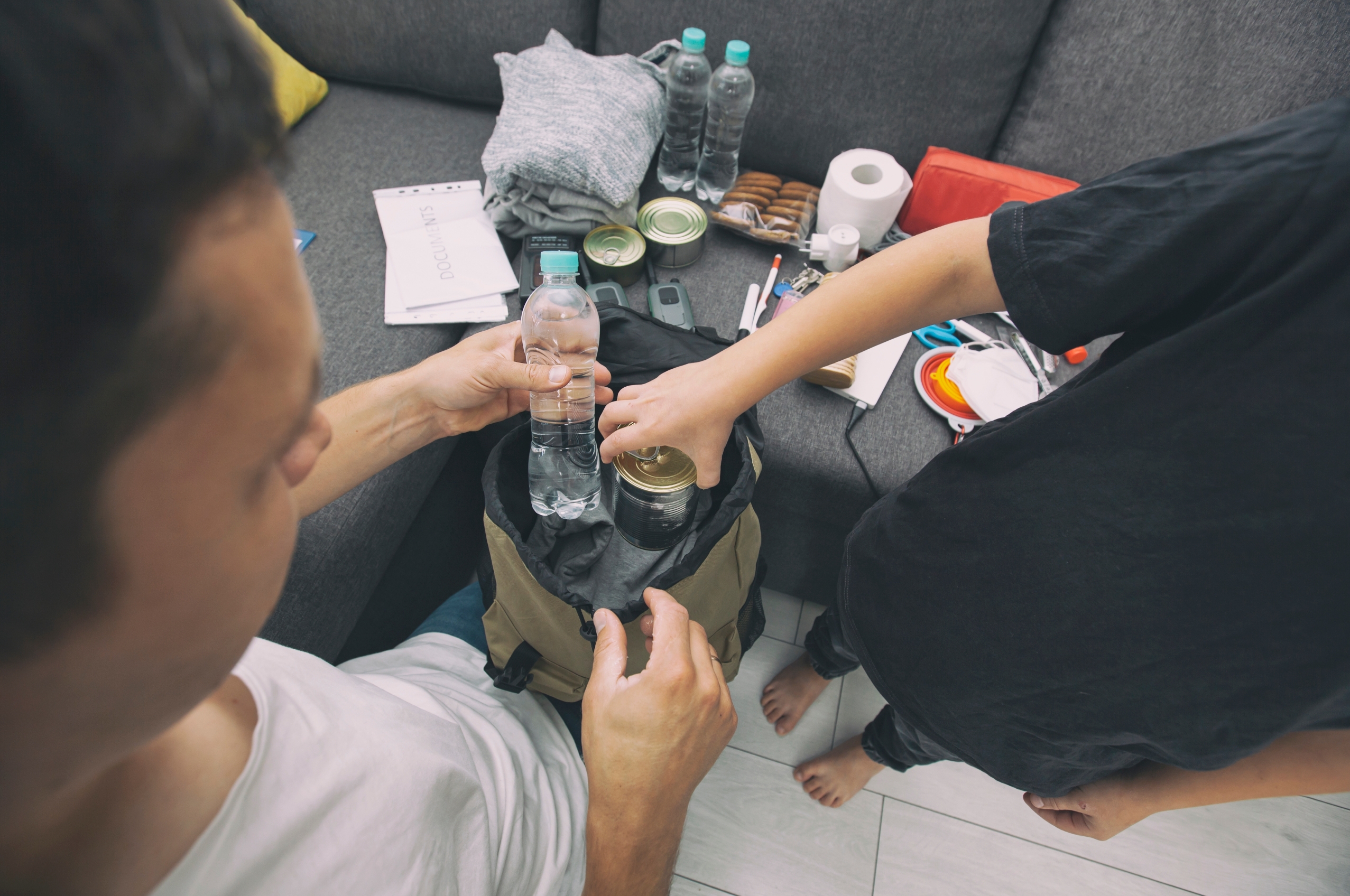 Two people preparing an emergency bag; one is holding a bottle of water and the other is securing a can.